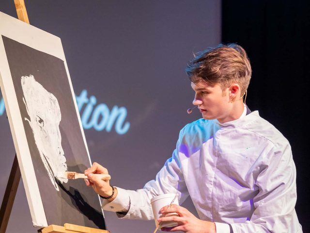 Vincent Frommer im weißen Kittel malt während der Show „Magie der Intuition“ auf eine Leinwand